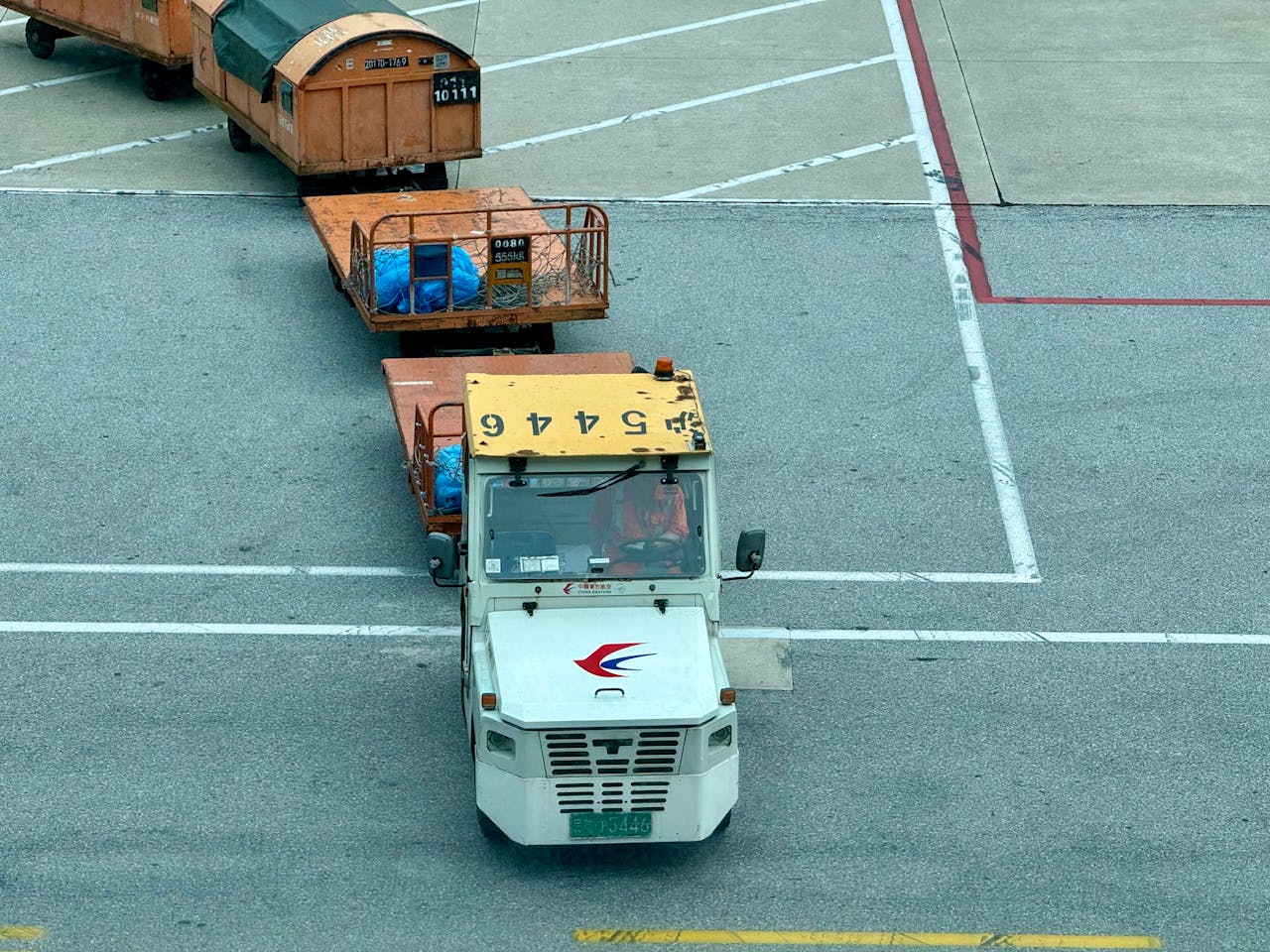 A tow tractor pulls cargo containers on an airport tarmac, showcasing aviation logistics.